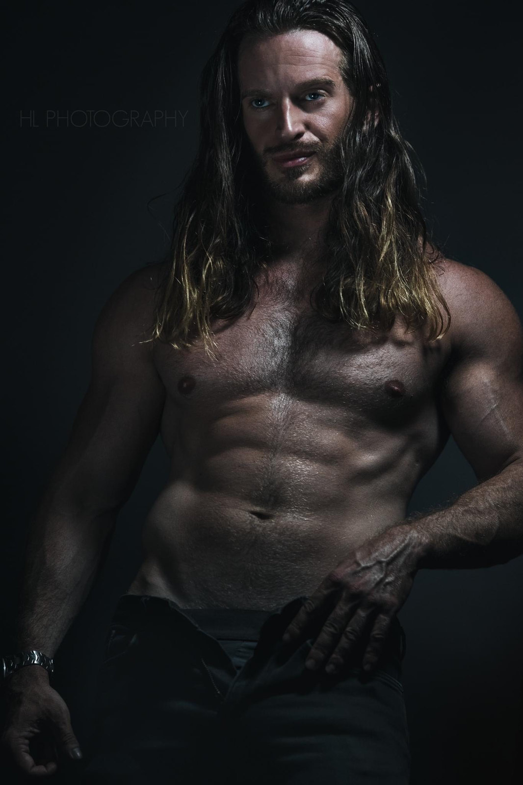Russell Snipes. Shirtless fitness portrait, long hair, dark backdrop