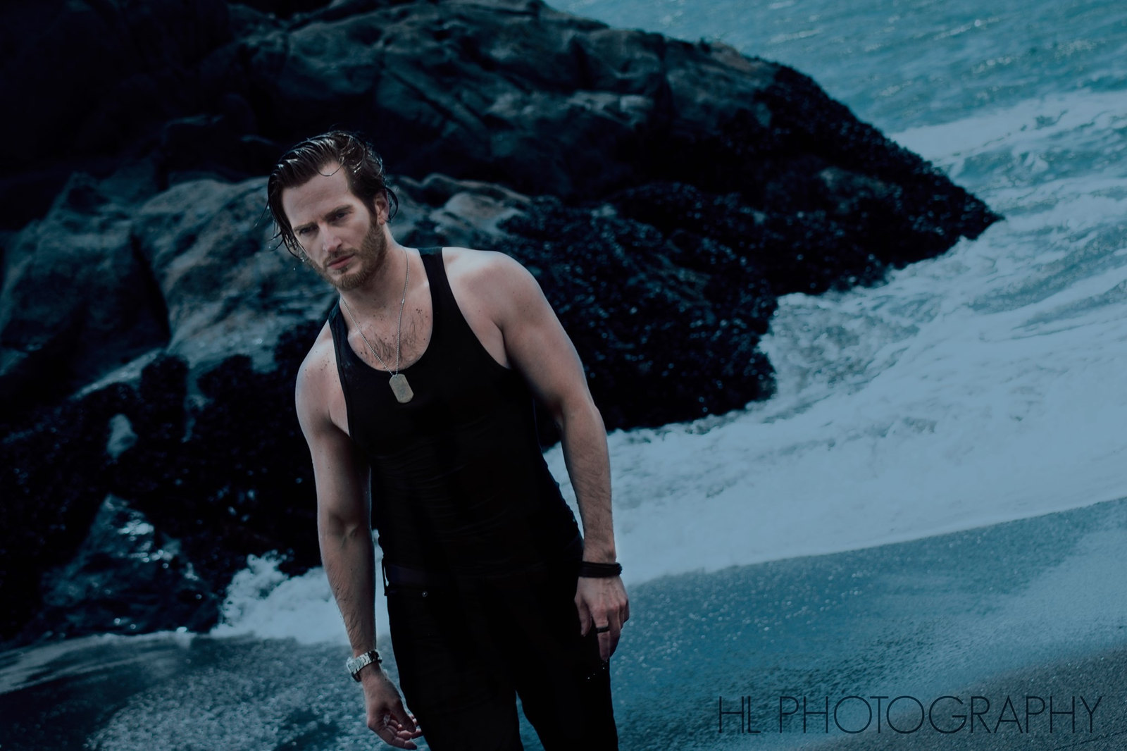 Russell Snipes. Lifestyle shot in a tank top on a rocky coastline