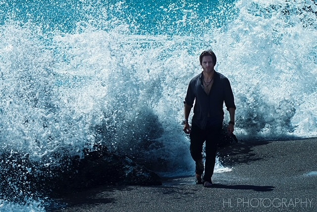 Russell Snipes. Wide shot walking on rocks by crashing ocean waves